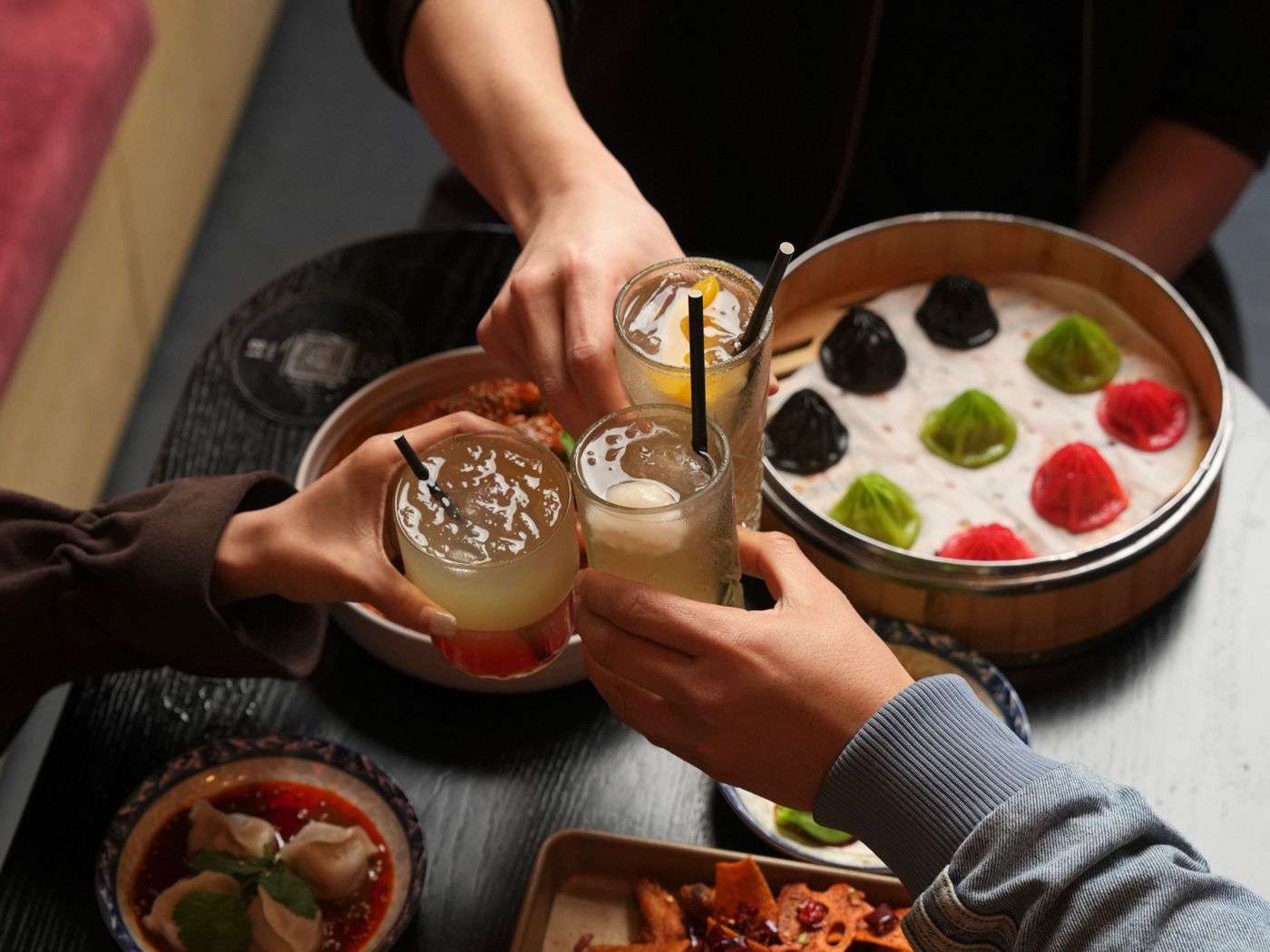 Friends clinking drinks over xiao long bao and chilli wings at Mr Hao